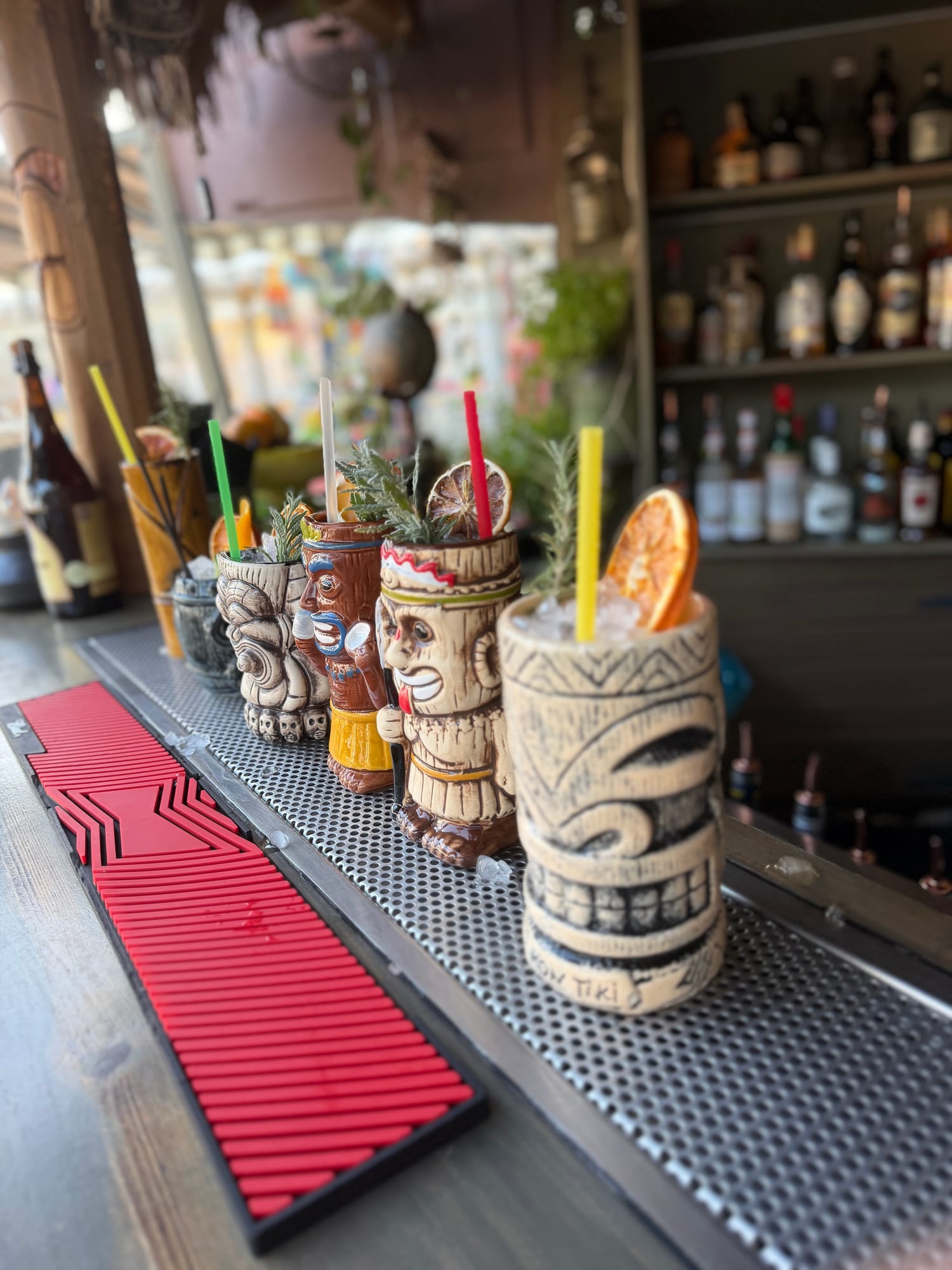 Five colourful tiki mugs lined up along the bar